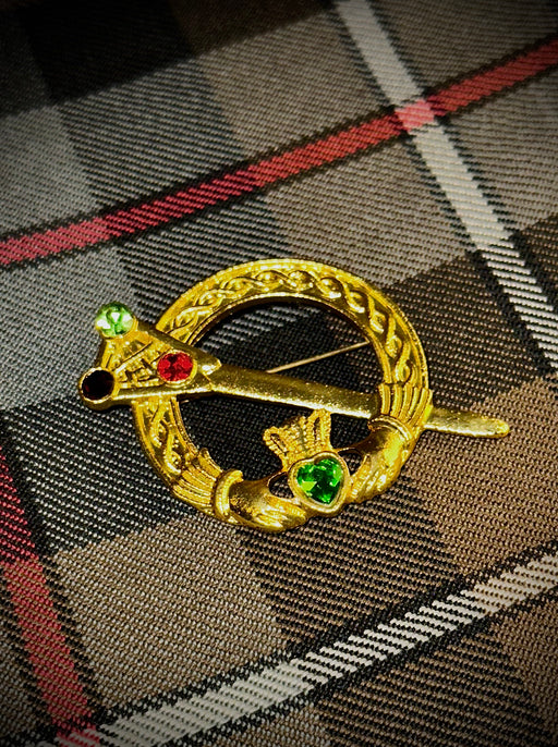 Golden Irish Tara Brooch with red, black and green gem stones. Weathered McKenzie tartan background. 