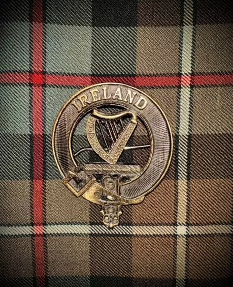 "Ireland" Kilt Pin in bronze colour. Harp in the center of Kilt Pin with Ireland written across the top. Background of weathered mckenzie tartan